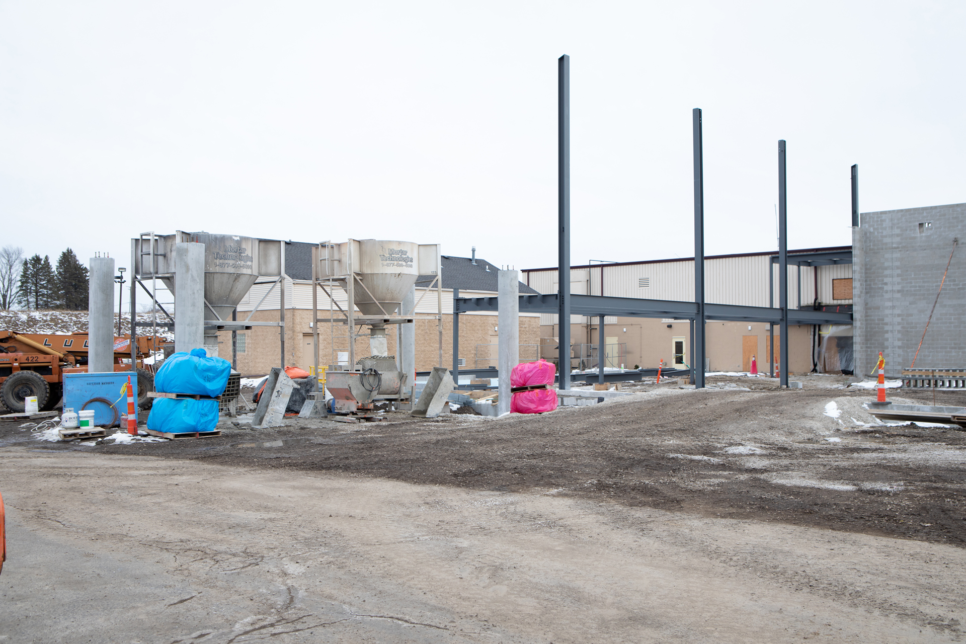 The 4 concrete columns will hold the drive under/drop off canopy. The 2 large “funnels” contain the mortar used by the masons. The tall vertical steel columns support the roof and separate the lobby from the classroom area. The shorter steel structure supports the mezzanine in the lobby.