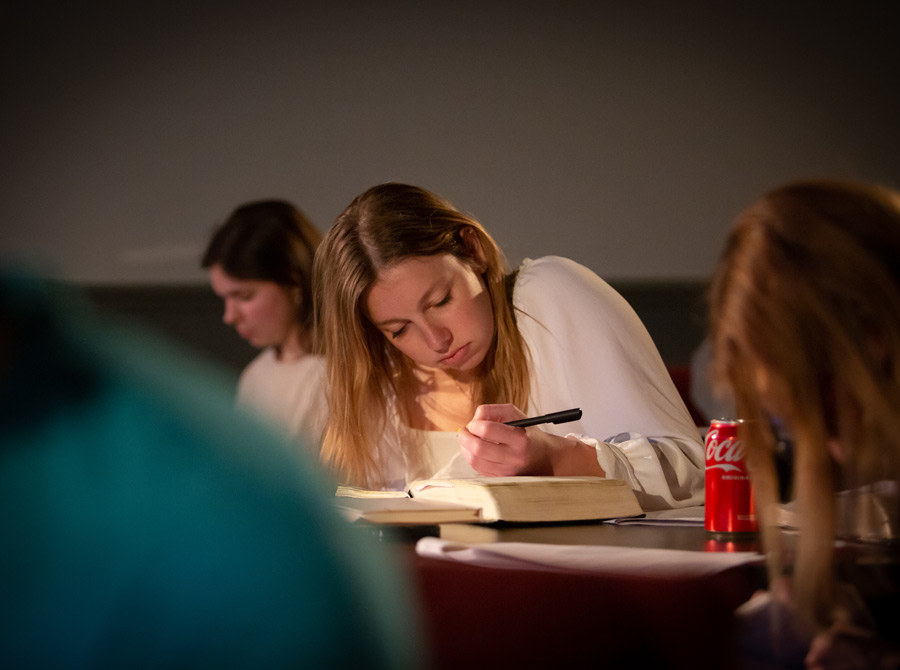 A girl takes notes and studies in her Bible while surrounded by others who do the same.