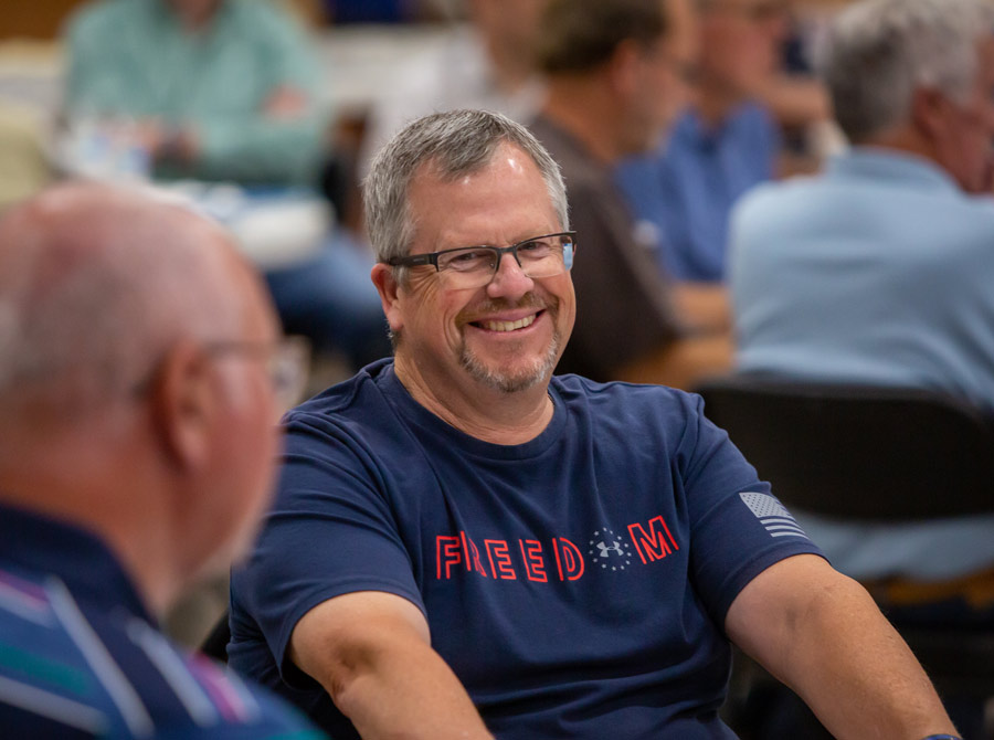 A man in the center of the photo smiles, enjoying the mens event he is attending.