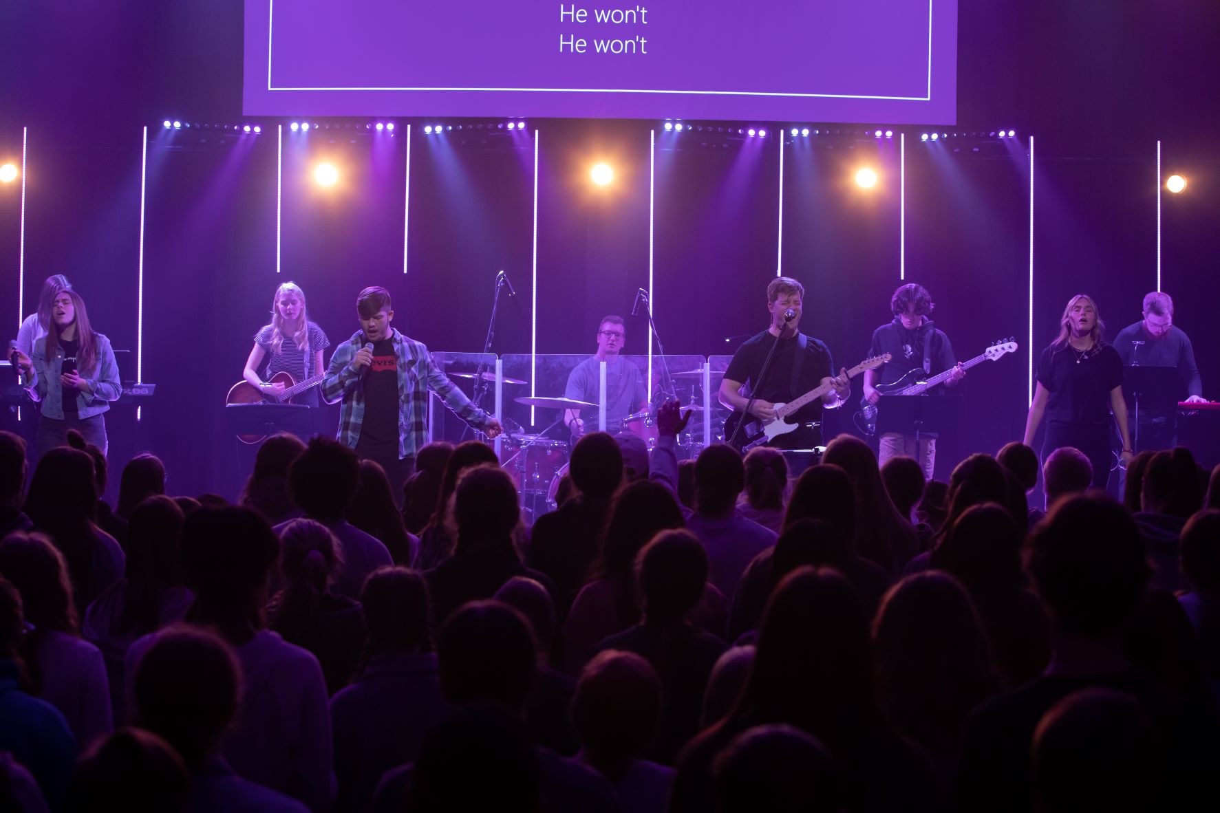 A band leads worship for many students in the foreground.