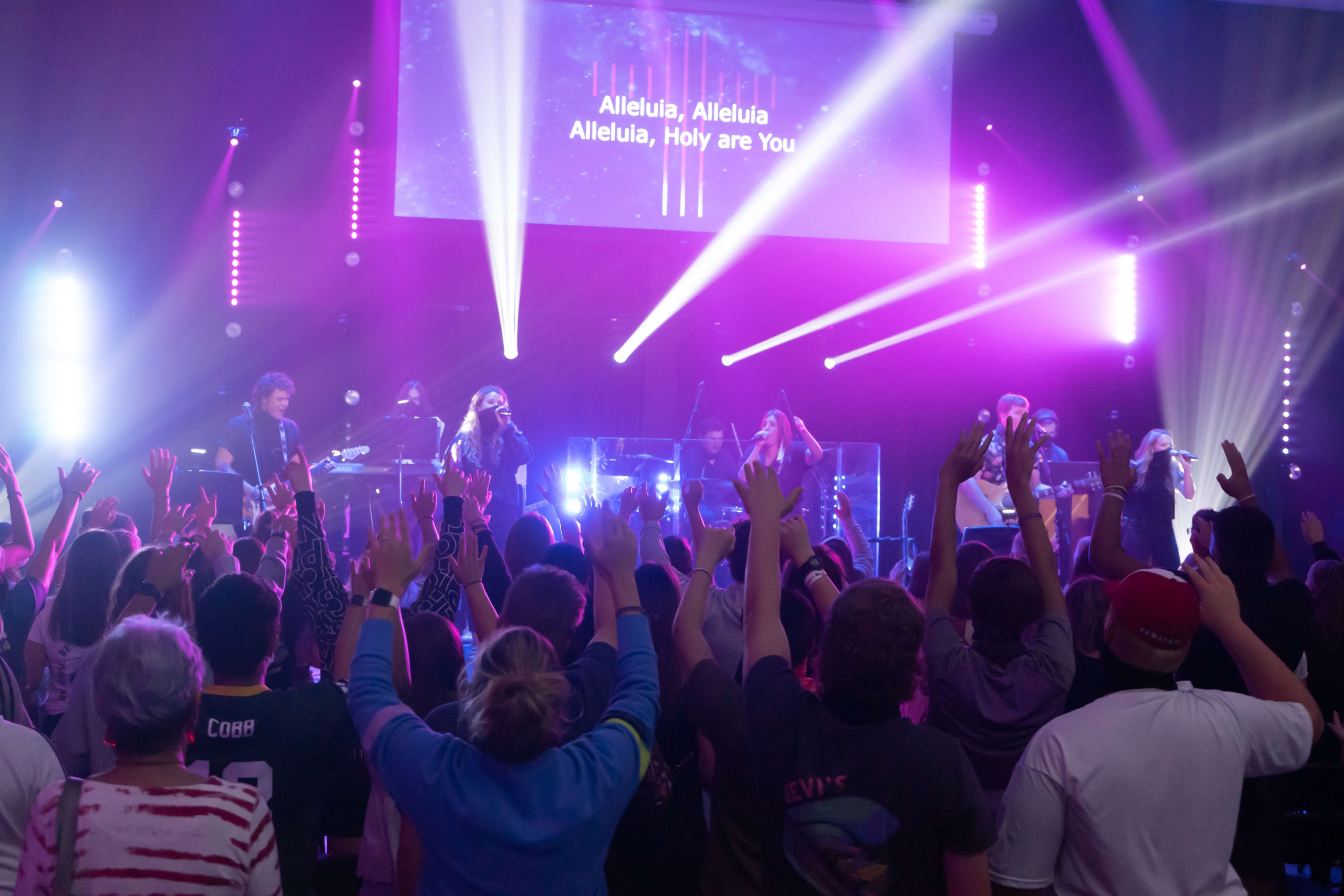 A large group of students raises their hands in worship during a worship night.