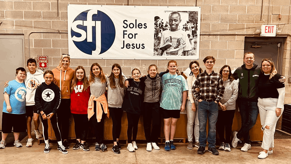 A group of volunteers smiles in front of the "Soles for Jesus" ministry which they are serving.