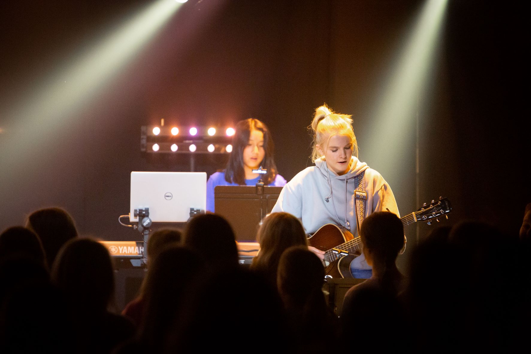 Two girls lead worship for many students in the foreground.